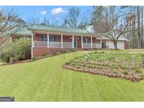 Charming brick home with a metal roof, white porch railing, and well-manicured lawn with garden bed at 81 Bowers Rd, Moreland, GA 30259
