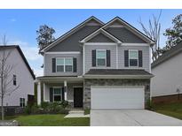 Charming two-story home with a gray exterior, stone accents, attached two car garage and a well manicured lawn at 9068 Jim Purcell Dr, Covington, GA 30014