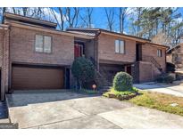 Inviting brick townhome featuring an attached garage, landscaped front, and covered stairwell leading to the front door at 5545 Circlestone Ln, Stone Mountain, GA 30083