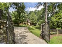 A gated entrance opens to a private drive leading to a charming home surrounded by lush landscaping at 6320 Nw Riverside Dr, Sandy Springs, GA 30328