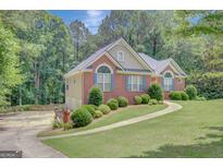 Charming brick home featuring arched windows, blue shutters, lush landscaping, and a winding sidewalk to the driveway at 140 Rockglen Ct, Fayetteville, GA 30215