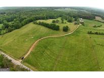 Expansive aerial view of green pastures, a winding driveway, and a charming farmhouse nestled among mature trees at 1761 Reavesville Rd, Bowdon, GA 30108