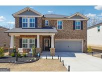Two-story home featuring stone accents, a two-car garage, manicured landscaping, and a welcoming covered front porch at 6910 Newcastle Ct, Fairburn, GA 30213