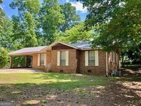 Quaint brick home with a metal roof, carport, and a spacious front yard surrounded by mature trees at 360 Meadowbrook Dr, Mcdonough, GA 30253