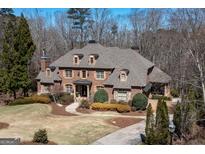 A brick two-story home with a manicured front lawn, a circular driveway, and mature trees in the background at 120 Kettering Trce, Tyrone, GA 30290