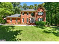 Beautiful two story brick home featuring a manicured lawn, lush trees, and a welcoming front entrance at 423 Holly Grove Church Rd, Peachtree City, GA 30269