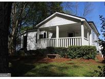 Charming single story home featuring a covered front porch, lush landscaping, and mature trees at 1 Maple St, Porterdale, GA 30014