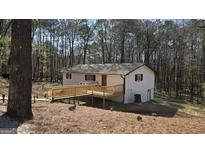 Charming home exterior featuring a wooden deck and a red front door, surrounded by a lush, wooded landscape at 3189 Fern Ridge Ne Dr, Conyers, GA 30013