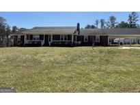 Ranch-style home featuring a brick exterior, covered porch, chimney, attached carport, and a spacious front yard at 130 Norman Rd, Covington, GA 30014