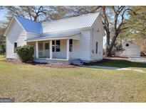 Charming one-story home with a covered porch and metal roof nestled among mature trees at 6316 Rockland Rd, Lithonia, GA 30038