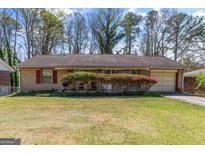 Charming brick ranch home with a manicured lawn, blossoming azaleas, and an attached garage at 447 Wavelyn Way, Riverdale, GA 30274