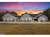 Stunning white brick home with black roof, green lawn, and picturesque sunset sky at 2615 Hampton Locust Grove Rd, Locust Grove, GA 30248