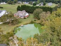 Expansive aerial view of a brick home with a private pond and lush landscaping at 557 Arrowhead Cir, Rutledge, GA 30663