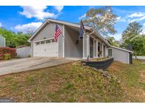 Charming home featuring a two-car garage and American flags, set against a backdrop of mature trees and sky at 205 Raintree Bnd, Peachtree City, GA 30269