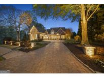 Stately home featuring a brick driveway, lush landscaping, and warm exterior lighting at 113 Regents Sq, Peachtree City, GA 30269