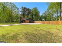 Modern dark exterior home with a spacious lawn, long driveway, and a classic wood fence at 608 E Banks Rd, Fayetteville, GA 30214