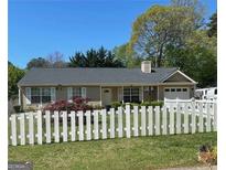 Charming one-story home with a well-manicured lawn and a classic white picket fence, surrounded by mature trees at 1081 Singleton Valley Cir, Norcross, GA 30093