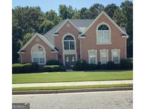 Charming brick home featuring a well-manicured lawn, manicured shrubbery, and a gray roof at 135 Danube Trl, Stockbridge, GA 30281