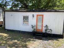 Charming tiny home featuring a bright orange front door and manicured front yard at 6052 Pine St, Austell, GA 30106
