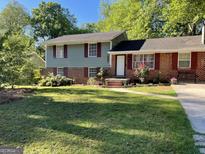 Split-level home featuring a well-manicured lawn, brick accents, and mature trees in a peaceful residential neighborhood at 77 Crystal River Dr, Riverdale, GA 30274