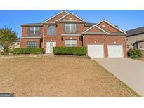 Two-story red brick home featuring an attached two-car garage and manicured landscaping at 3971 Busby Mill Ct, Ellenwood, GA 30294
