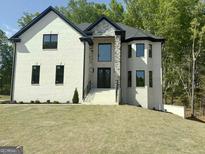 Elegant two-story home featuring a white brick facade, stone accents, a manicured lawn, and a striking black roof at 409 Saint Surrey Way, Ellenwood, GA 30294