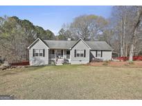 Charming single-story home featuring gray siding, black shutters, and a cozy front porch with an American flag at 100 Rockland Trl, Sharpsburg, GA 30277