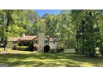 Traditional home featuring a well-maintained lawn and mature trees, with a brick chimney and charming front porch at 15 Perthshire Dr, Peachtree City, GA 30269