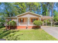 Charming single-story home with a covered porch and a carport, surrounded by lush greenery and a well-maintained lawn at 842 Brighton Dr, Lawrenceville, GA 30043