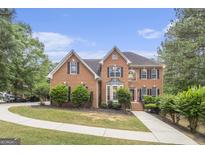 Traditional brick home featuring a manicured lawn, mature trees, and a charming red front door at 1085 Crown River Pkwy, Mcdonough, GA 30252