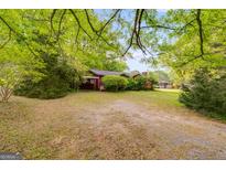 View of the front yard and exterior of the red home surrounded by mature trees and landscaping at 362 Highway 113, Temple, GA 30179