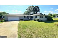 Charming one-story home with an attached garage, green lawn, and an American flag at 140 Whitehead Sw Rd, Oxford, GA 30054