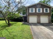 Charming two-story home features a lush front yard, a two-car garage, and classic architectural details at 4457 Huntshire Dr, Stone Mountain, GA 30083