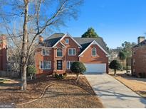 Traditional red brick two-story home with a two-car garage, manicured lawn, and mature trees on a sunny day at 4683 Heritage Lakes Sw Ct, Mableton, GA 30126