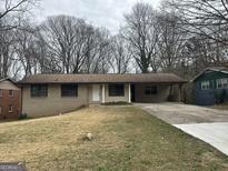 Single-story home features a light brick exterior, covered parking, and a well-maintained front lawn at 6982 Knollwood Dr, Morrow, GA 30260