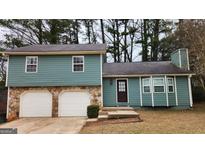 Split level home with a stone base, garage, and front door surrounded by green grass and trees at 5128 Running Fox Trl, Norcross, GA 30071