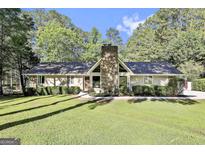 Charming single-story home with a stone chimney, mature trees, and a well-manicured lawn at 180 Willow Lake Ln, Sharpsburg, GA 30277