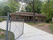Charming brick home featuring a classic design and an expansive concrete driveway, all enclosed by a secure chain-link fence at 8145 Attleboro Dr, Jonesboro, GA 30238