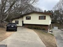 Split-level home with brick foundation, cream siding, brown trim, and a concrete driveway surrounded by trees at 2195 Wilson Nw Rd, Conyers, GA 30012