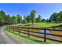 Scenic pond with a wooden fence surrounded by lush greenery and a clear blue sky in a beautiful landscape at 228 Indian Creek Rd, Locust Grove, GA 30248