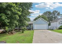 Charming, light blue single-story home featuring a two-car garage, manicured lawn and lush trees at 1152 Sunday Ln, Jonesboro, GA 30238