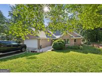 Inviting brick home featuring an attached garage, green lawn, mature trees, and a large driveway at 4333 Deer Ridge Ct, Lilburn, GA 30047
