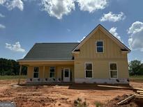 New construction home featuring yellow siding, a covered porch, and a dark roof against a bright blue sky at 242 Old Jackson Rd, Mcdonough, GA 30252