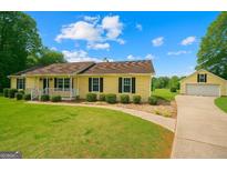 Charming yellow house with black shutters, manicured front lawn, and detached two-car garage at 183 Brookwood Estates Trl, Stockbridge, GA 30281