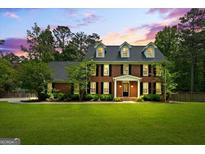 Elegant two-story brick home with a manicured lawn, black shutters, and dormer windows under a beautiful sunset sky at 171 Ponderosa Drive, Fayetteville, GA 30214