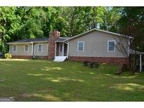 Charming ranch-style home with a brick chimney and well-maintained lawn surrounded by lush greenery at 142 Carrollwood Dr, Fayetteville, GA 30215