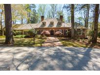 Charming brick home featuring a wood roof, dormer windows, mature trees, and a welcoming brick walkway at 9995 Huntcliff Trce, Atlanta, GA 30350