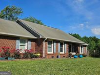 Charming brick home featuring a well-manicured lawn, blue shutters, and colorful potted plants at 2585 Old Jackson Rd, Locust Grove, GA 30248