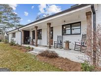 Charming white brick home featuring a rocking chair front porch with rustic wood columns at 4739 Lower Jersey Rd, Oxford, GA 30054