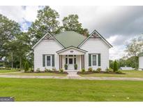 Charming white cottage with green metal roof, decorative shutters, and lush landscaped front yard at 111 S Old 27, Roopville, GA 30170